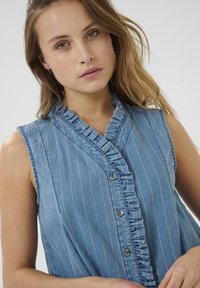 Zila denima bez piedurknēm kleita ar vertikālām baltām svītrām, plīvurotu apdari un pieciem pogu aizdariem. Mīksta tekstūra un pieguļošs dizains.