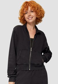Czarna bluza z suwakiem, wykonana z miękkiego materiału, z wysokim kołnierzem, kieszeniami z przodu i ściągaczami przy mankietach. Luźny krój o prostym designie.