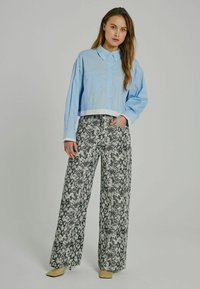 Camicia button-up azzurra corta con tasca sul petto; pantaloni a palazzo neri e bianchi con stampa rettile a vita alta; tacchi beige.