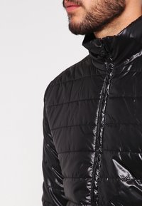 Black padded jacket featuring a high collar, shiny finish, and horizontal quilted pattern, with a partial front zipper for closure.