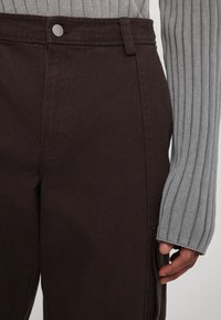 Ruskeat puuvillaiset cargohousut, joissa on korkeavyötärö, näkyvä nappi, sivutaskut ja teksturoitu harmaa ribbineuloshiha.