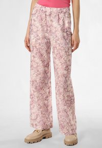 Leichte, rosa gemusterte Schlaghosen mit elastischem Bund, aus einem weichen Stoff gefertigt, kombiniert mit beigen Schuhen mit dicker Sohle.