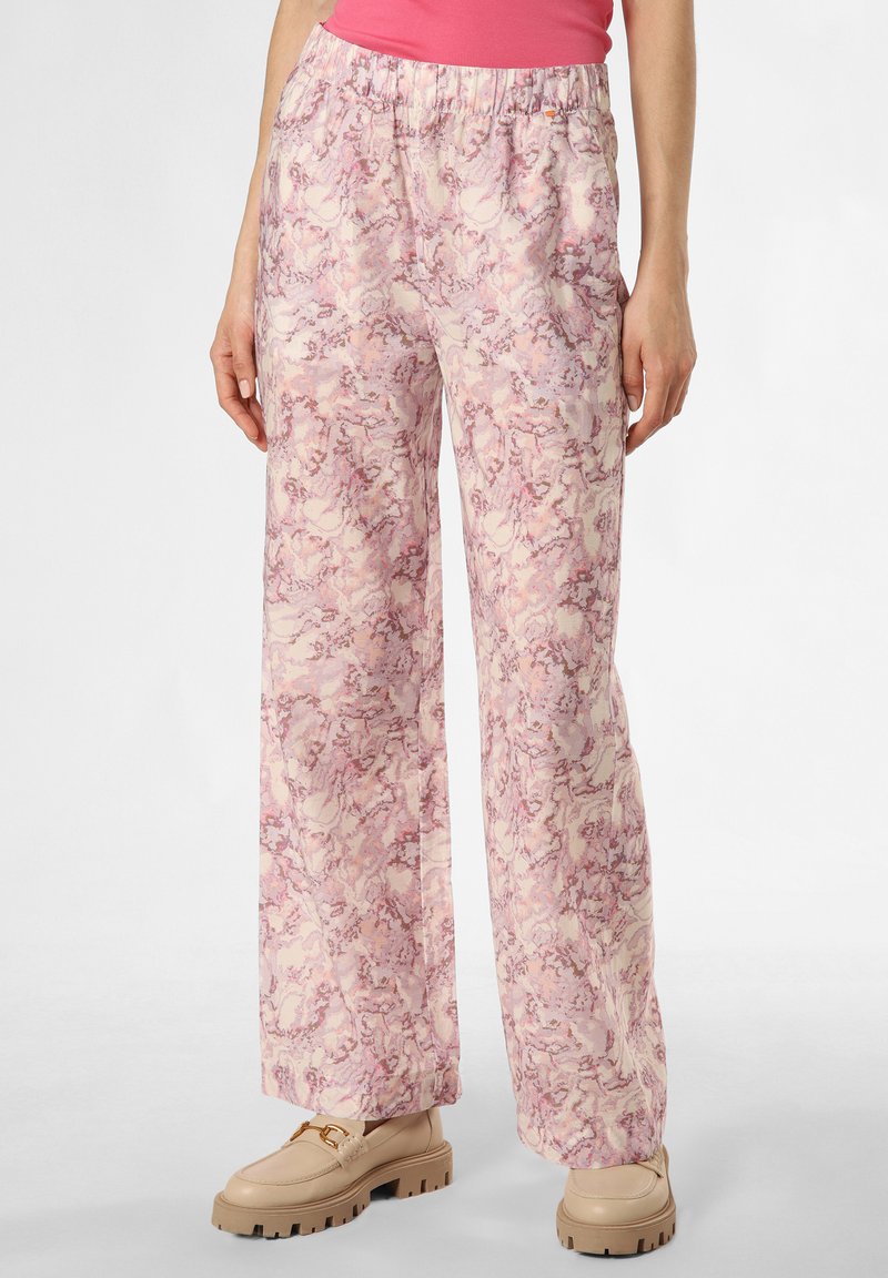 Leichte, rosa gemusterte Schlaghosen mit elastischem Bund, aus einem weichen Stoff gefertigt, kombiniert mit beigen Schuhen mit dicker Sohle.