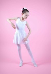 Weißes Ballettkleid mit einem transparenten Rock, kombiniert mit weißen Strumpfhosen und Ballettschuhen. Die Haare sind mit einer weißen Schleife frisiert. Der Hintergrund ist pink.