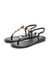 Črne ravne sandale s thong dizajnom, ki vsebujejo kovinske okrasne diskete vzdolž traku. Podplat je gladek in preprost, z nastavljivimi gležnjastimi trakovi.
