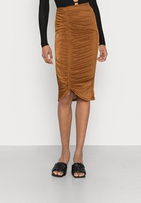 Saia midi de cor ferrugem com design franzido, feita de tecido suave, apresentando uma bainha com fenda. Combinada com sandálias de slide trançadas pretas.