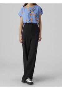 Blusa blu a maniche corte con motivo floreale arancione, abbinata a pantaloni neri a vita alta e gamba larga e scarpe basse argento.
