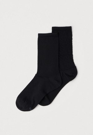 Due paia di calzini neri: uno con una texture liscia e un bordo a costine, l'altro con un motivo testurizzato lungo un lato.