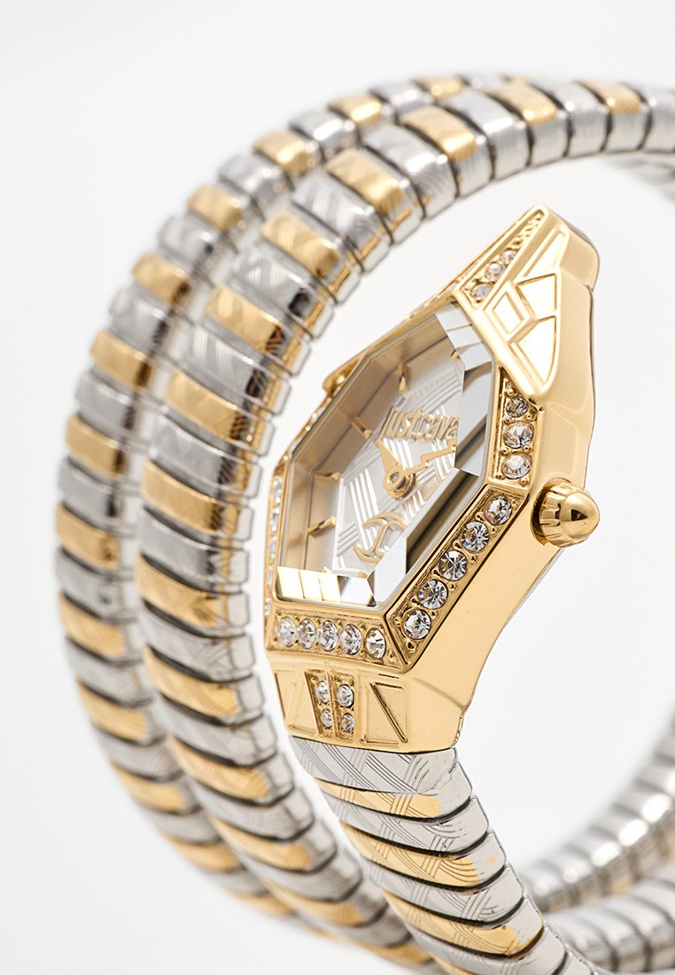 Orologio in oro e argento con quadrante ottagonale, decorazioni in cristallo e cinturini texturizzati che creano un design intrecciato.