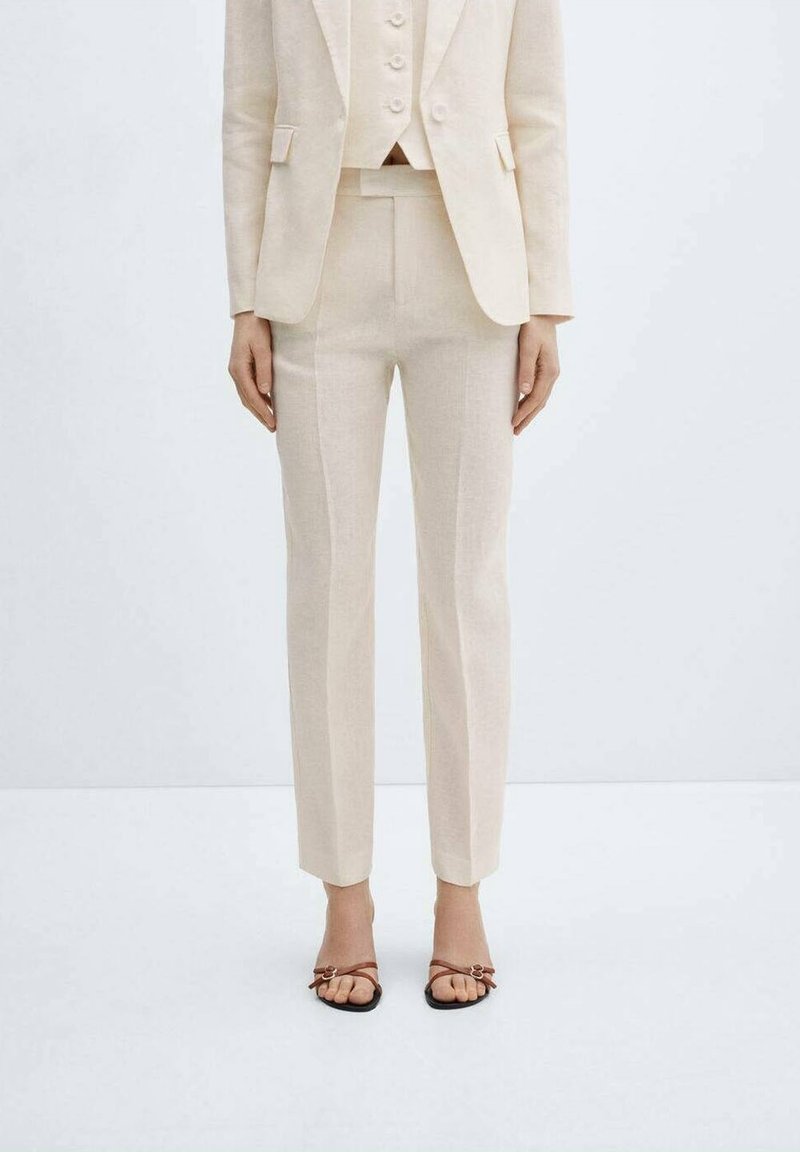 Costume en lin beige composé d'une veste cintrée, d'un gilet assorti et d'un pantalon slim. Accompagné de sandales à brides avec un détail subtil de boucle.