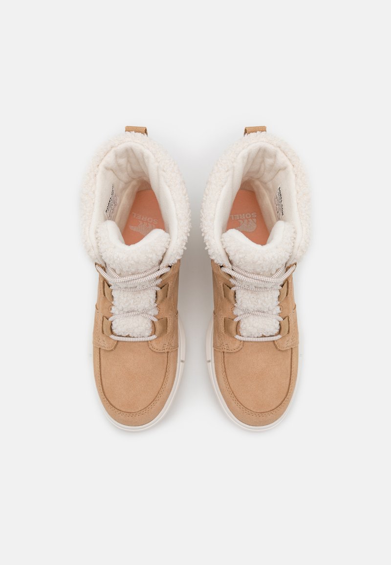 Chaussures montantes en suède beige avec un col en fourrure blanche, des lacets blancs et une semelle en caoutchouc. Présente un logo sur la semelle intérieure.