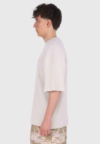 Lys beige ribbet kortærmet t-shirt med en afslappet pasform. Har en rund halsudskæring og diskret branding på brystet. Båret med camo-shorts.