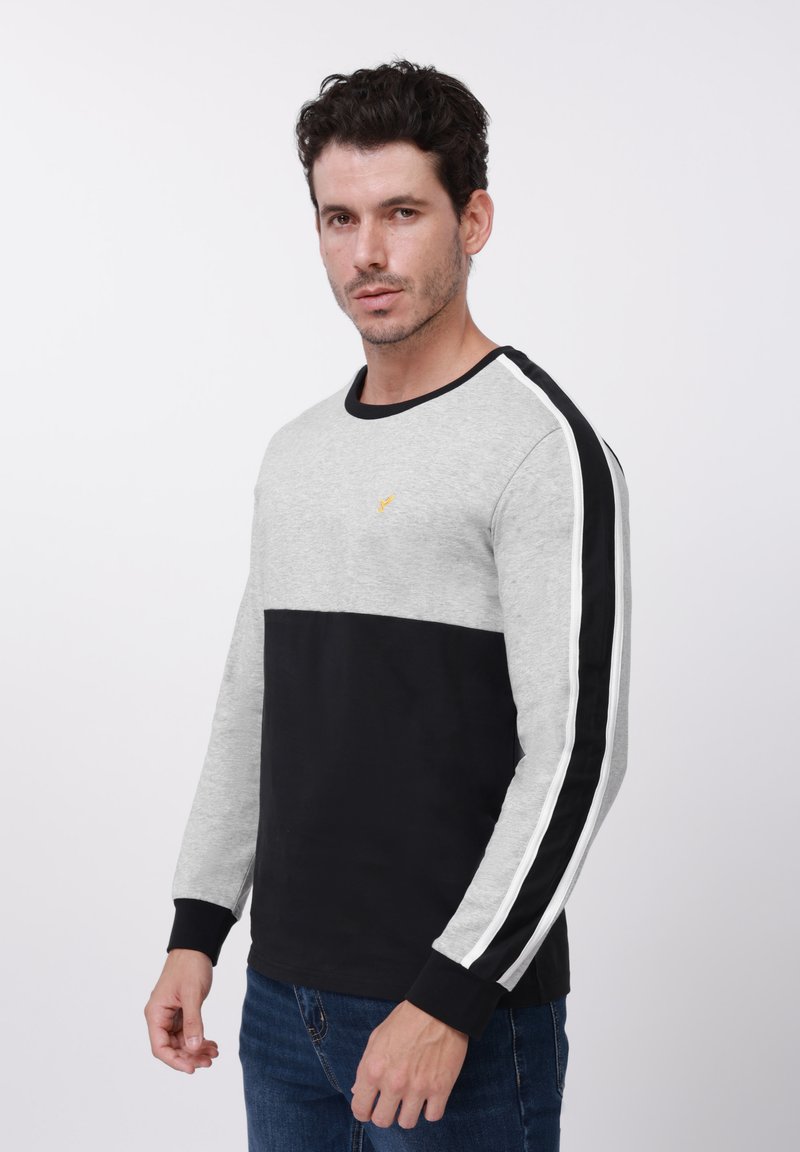 Siva i crna majica dugih rukava s okruglim izrezom, s donjim dijelom u čvrstoj crnoj boji i bijelim bočnim prugama. Uočljiv detalj žutog logotipa.