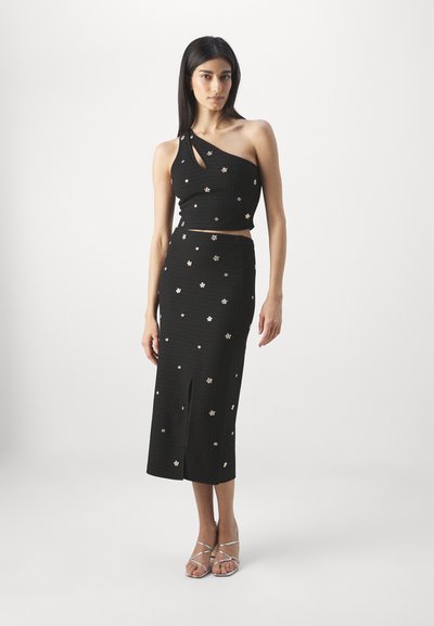 Ensemble noir en deux pièces composé d'un top asymétrique et d'une jupe midi, décoré de petites accents floraux dorés et d'une fente sur le devant.