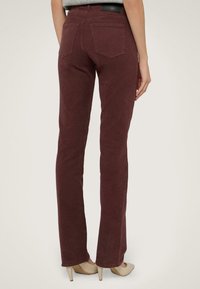 Pantalones de campana burdeos con una textura suave, que cuentan con dos bolsillos traseros y una etiqueta en la cintura. Combinados con unos tacones altos beiges.