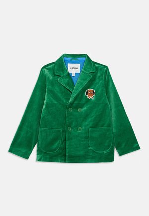 Blazer croisé en velours vert avec larges revers, deux poches avant et un petit écusson brodé en forme de chien marron sur la poitrine.