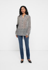 Black and white patterned blouse with a loose fit, button-up front, and long sleeves, paired with blue jeans and black heels.