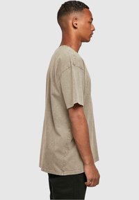 Khaki oversized majica od mekog, teksturiranog materijala. Okrugli izrez i kratki rukavi, s vidljivim detaljima šivanja. Jednostavan i ležeran dizajn.