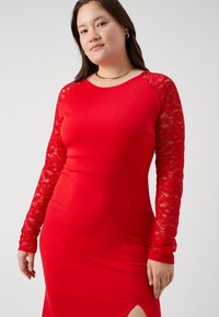 Červené šaty s dlhými čipkovými rukávmi, priliehavým telom a bočným rozparkom na leme. Hladká tkanina s elegantným siluetou.