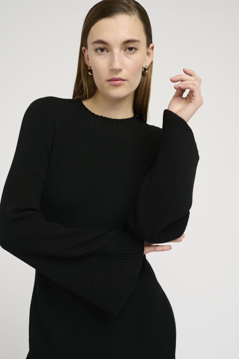 Black ribbed knit sweater with long flared sleeves and a round neckline, featuring a textured fabric and fitted design.