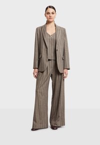 Completo a righe marroni con giacca oversize e pantaloni a gamba larga. Il tessuto ha una superficie liscia con una leggera lucentezza, completato da un top aderente.