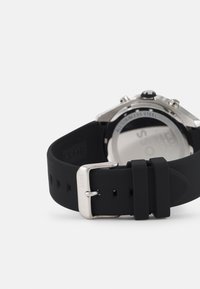 Black silicone strap watch with stainless steel hardware, featuring a smooth, matte texture and visible branding on the buckle.