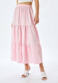 Gonna a strati rosa realizzata in un tessuto morbido con vita elasticizzata, caratterizzata da un design fluido e una leggera lucentezza. Abbinata a mule con tacco aperto bianche.
