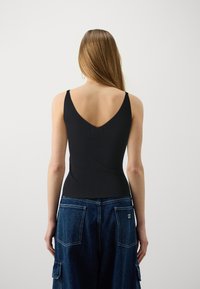 Camiseta negra de canalé con diseño de espalda en V profunda. Combinada con pantalones cargo de mezclilla azul que cuentan con grandes bolsillos traseros y una etiqueta.