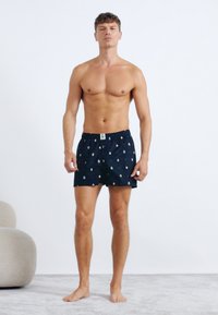 Marineblå boxer shorts med et prikket mønster. Fremstillet af letvægtsstof, med en elastisk talje og et lille label foran.