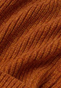 Nahaufnahme eines rostorangefarbenen gestrickten Wollstoffs, der eine gerippte Textur mit weichen, flauschigen Fasern und erhöhten vertikalen Stichen zeigt.