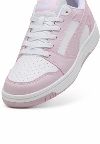 White and light pink sneaker with perforated toe box, smooth leather, and rubber outsole. Features white laces and accents on the side.