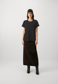 Camiseta negra de manga corta combinada con una larga falda de mezclilla marrón y botas negras hasta el tobillo. El conjunto se complementa con una gorra verde oscuro.