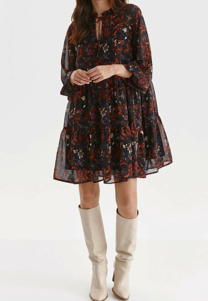 Svart blommig klänning med flödande silhuett, med rundad halsringning och långa ärmar. Accenterad med ett repknut och bärs med knähöga beiga stövlar.