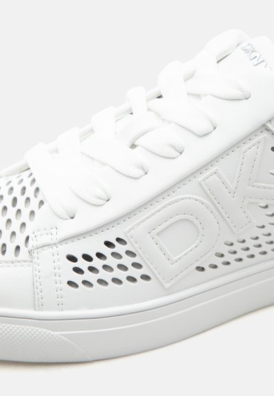 Baskets blanches avec un design perforé, lacets blancs, et logo "DKNY" en relief sur le côté, vues en gros plan du côté extérieur.