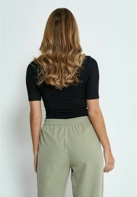 Top negro ajustado con mangas cortas, combinado con pantalones de cintura elástica de color verde claro. Cabello largo y ondulado cae por la espalda.