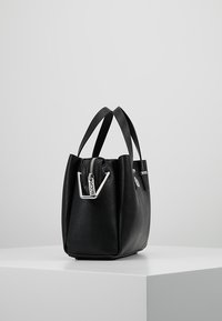 Musta nahkakotelo teksturoidulla pinnalla, yläkahvoilla, hopeasella vetoketjulla ja minimalistisella suunnittelulla. Kompakti, rakenteellinen muoto.