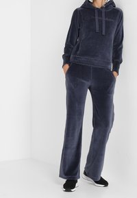 Navy Velours-Hoodie mit Fronttasche und Kordelzug, kombiniert mit passenden, lässig geschnittenen Hosen mit Seitentaschen und einer weichen Textur.