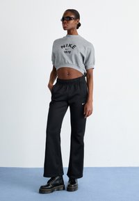 Sweatshirt cinzado com estampado preto "Nike 1972", combinado com calças de moletom pretas com cintura elástica e logótipo da Nike. Botas pretas de plataforma.