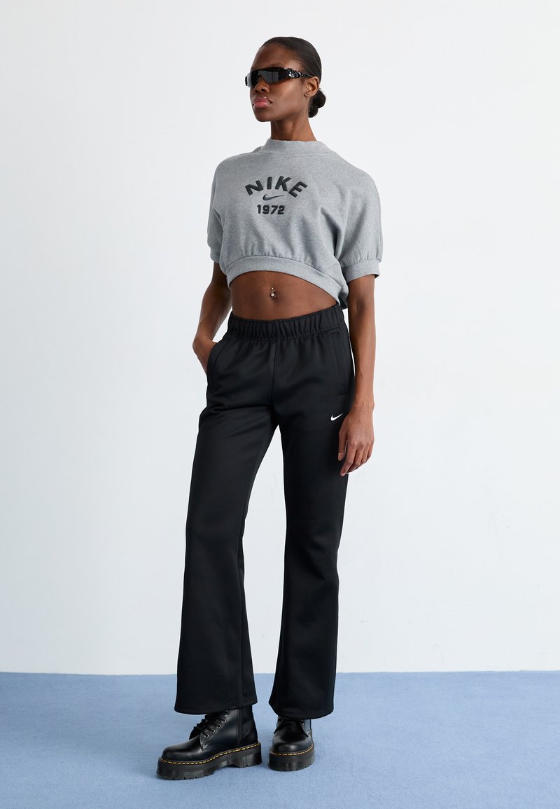 Felpa grigia corta con stampa nera "Nike 1972", abbinata a pantaloni joggers neri con vita elastica e logo Nike. Stivali neri con tacco alto.
