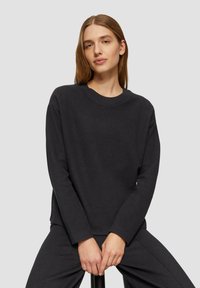Donkere grijze sweatshirt met ronde halslijn, lange mouwen en ribbeldetails. Zachte textuur en een ontspannen pasvorm. Gecombineerd met bijpassende donkere broek.