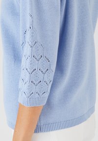 Maglione azzurro chiaro lavorato a maglia con un motivo in pizzo sulle maniche a tre quarti e dettagli a coste sui polsini e sull'orlo.