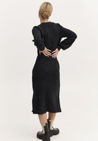 Abito nero lavorato a maglia con maniche lunghe, tessuto testurizzato, lungo fino al ginocchio, con orlo leggermente arricciato e indossato con stivali neri chunky.