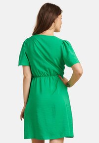 Groene jurk met korte mouwen, gemaakt van een glanzende, lichte stof. Heeft een aangeknoopte taille en een eenvoudige ronde halslijn. Soepele textuur.