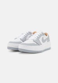 Weiße Ledersneaker mit grauen Akzenten, perforierter Zehenbox, flachen weißen Schnürsenkeln und einer dicken Gummisohle mit subtiler gestreifter Textur.