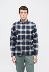 Marineblaues karierte Hemd zum Knöpfen mit weißer und grüner Einfassung, langen Ärmeln und Tasche; kombiniert mit grauer Hose. Baumwollmischgewebe, lockere Passform.