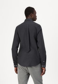 Donkergrijze langemouwen shirt met een kraag, knoopmanchetten en een rugplooidetail. Gemaakt van textuurstof, heeft het een getailleerde pasvorm en een gebogen zoom.