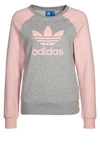 Ljusgrå sweatshirt med rosa raglanärmar. Har en stor rosa Adidas-logotyp på framsidan. Tillverkad av mjukt tyg med ribbade muddar.