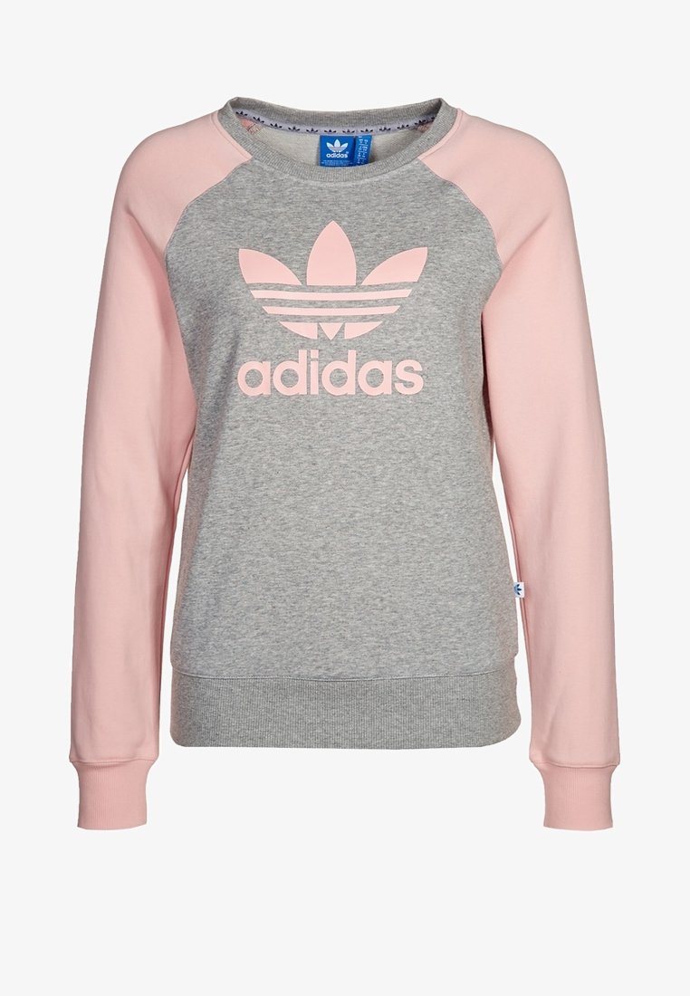 Vaaleanharmaa collegepaita, jossa on vaaleanpunaiset raglanhihat. Edessä suuri vaaleanpunainen Adidas-logo. Valmistettu pehmeästä kankaasta, jossa on resorit hihansuuissa.