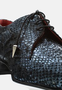 Zwarte leren dress shoe met reptielenprint materiaal, voorzien van een puntige neus, veters en een metalen accent nabij de veteropening.