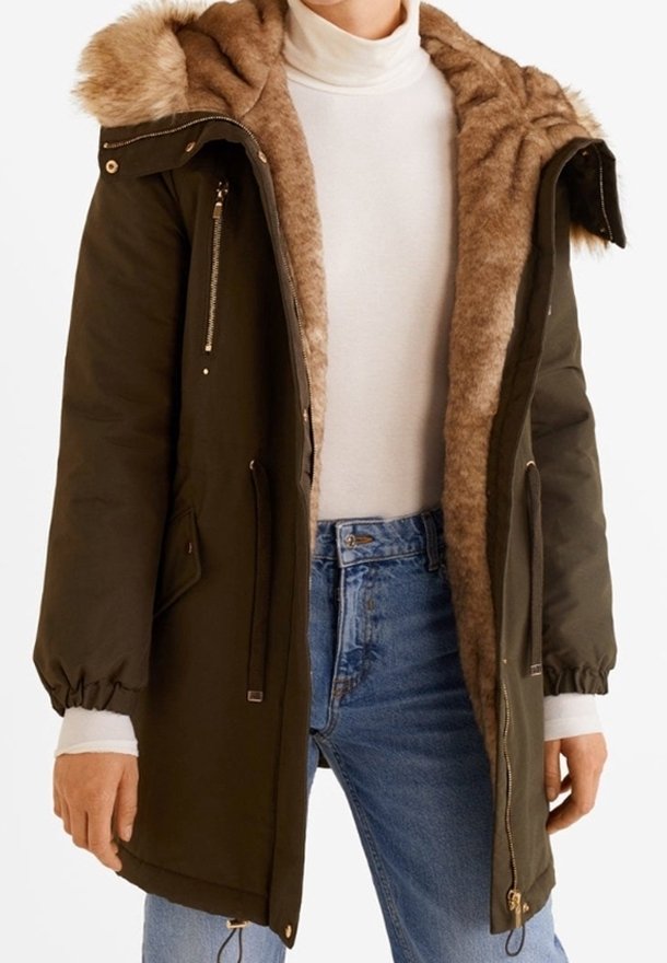 Parka femme vert olive avec capuche et intérieur en fourrure, portée ouverte sur un col roulé blanc et un jean bleu.
